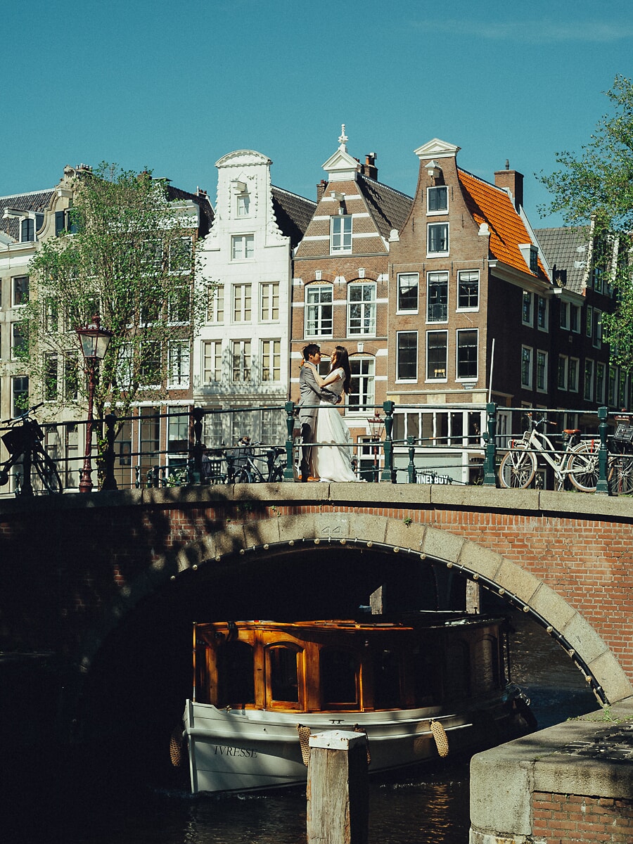 Wedding Bridal SP20 Pasgetrouwden omhelzen elkaar op een brug voor de grachtengevels, met een salonboot eronder, van een trouwfotograaf in Amsterdam