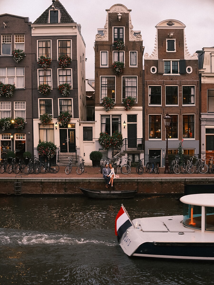 Wedding Bridal SP3 Onder gevels vol bloemen zitten ze aan de gracht terwijl een boot passeert, een filmisch beeld van een trouwfotograaf in Amsterdam