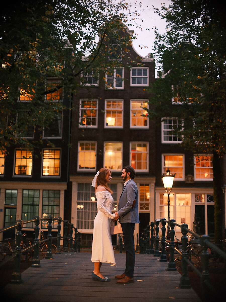 Wedding Bridal SP7 Tegenover elkaar op een grachtenbrug in de schemering met warm licht uit de ramen, een teder beeld uit de bruidssessie