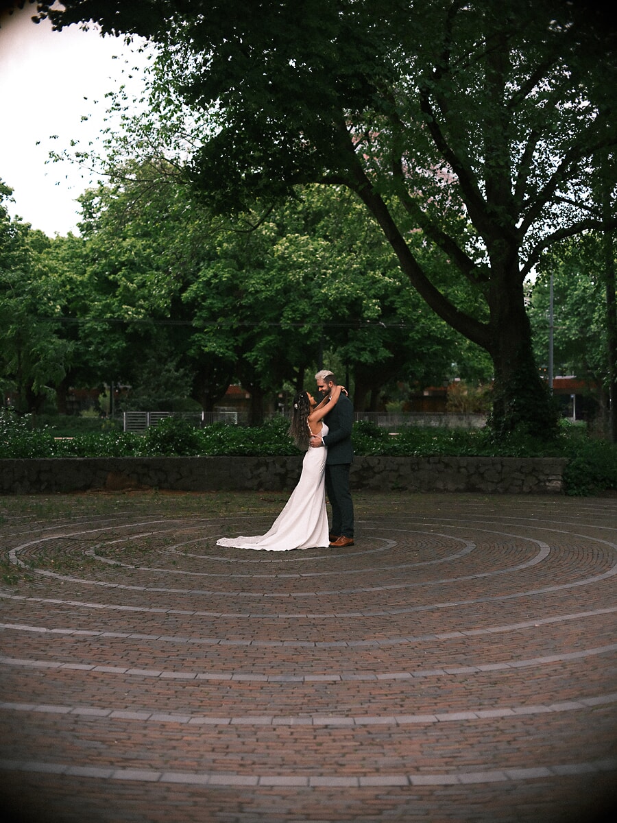 Wedding Bridal SP9 Stel omhelst elkaar midden in een rond bakstenen doolhof, de sleep uitgewaaierd over de stenen, een dromerig bruidsportret