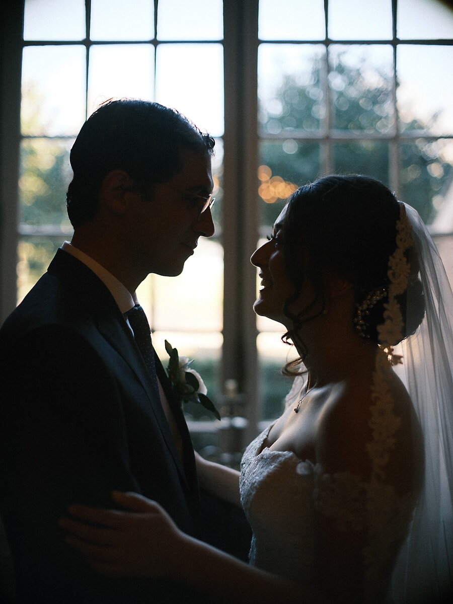 Wedding Bridal SP21 In silhouet voor hoge boogramen staan ze tegenover elkaar terwijl licht de kanten sluier vangt, een filmisch bruidsportret