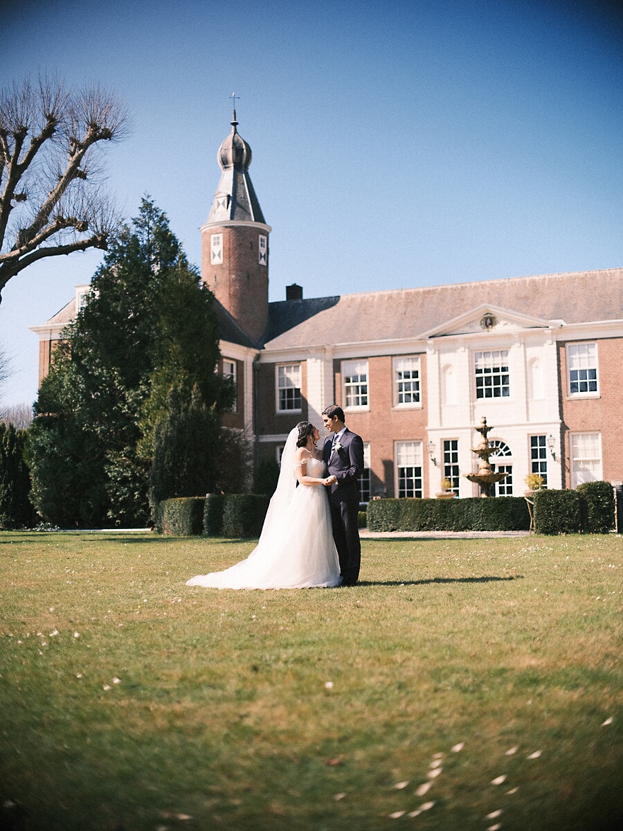Wedding Bridal SP22 Hand in hand op het gazon van een Nederlands landhuis onder een blauwe lucht poseert het stel voor een trouwfotograaf in Amsterdam
