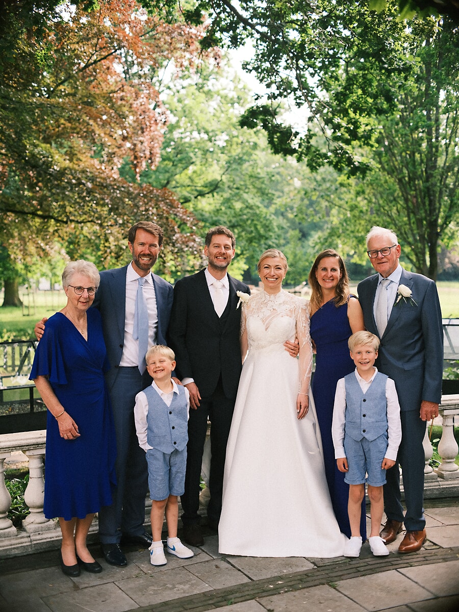 Wedding SP20 Bruid en bruidegom poseren met ouders en twee jongens in bijpassend blauw op een terras in het park, een warm familieportret