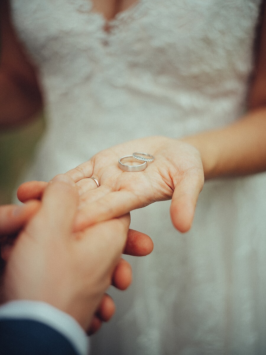 Wedding SP28 Close-up van de bruid met een trouwring in haar open handpalm boven de hand van haar bruidegom, een intiem ringdetail