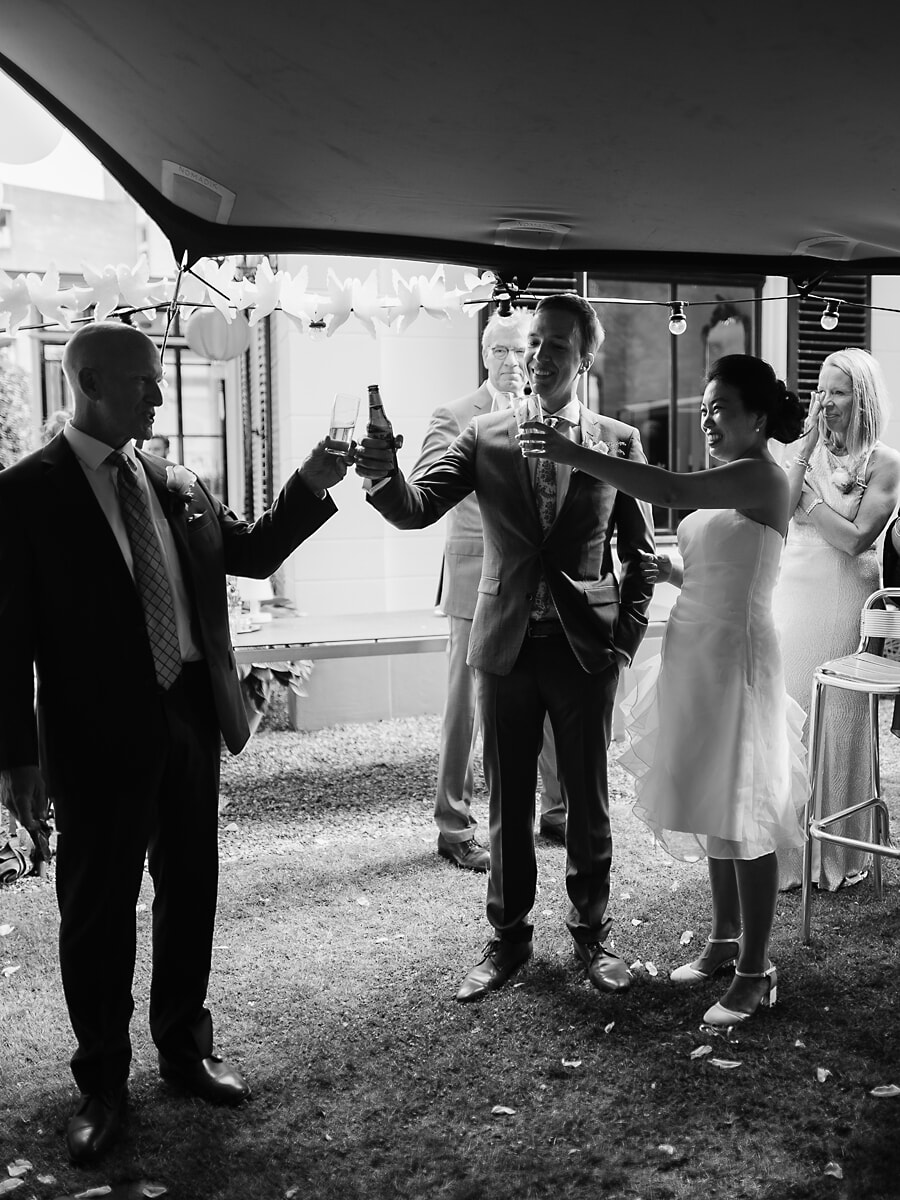 Wedding SP42 In zwart-wit proost het stel met de gasten onder de lampionnen, een warm moment van een trouwfotograaf in Amsterdam