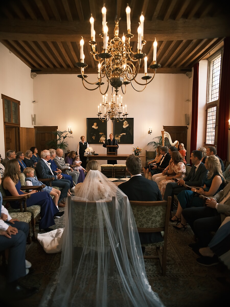 Wedding SP9 Achter de lange sluier van de bruid ontvouwt de ceremonie zich bij kaarslicht, een sfeervol beeld van een trouwfotograaf in Amsterdam
