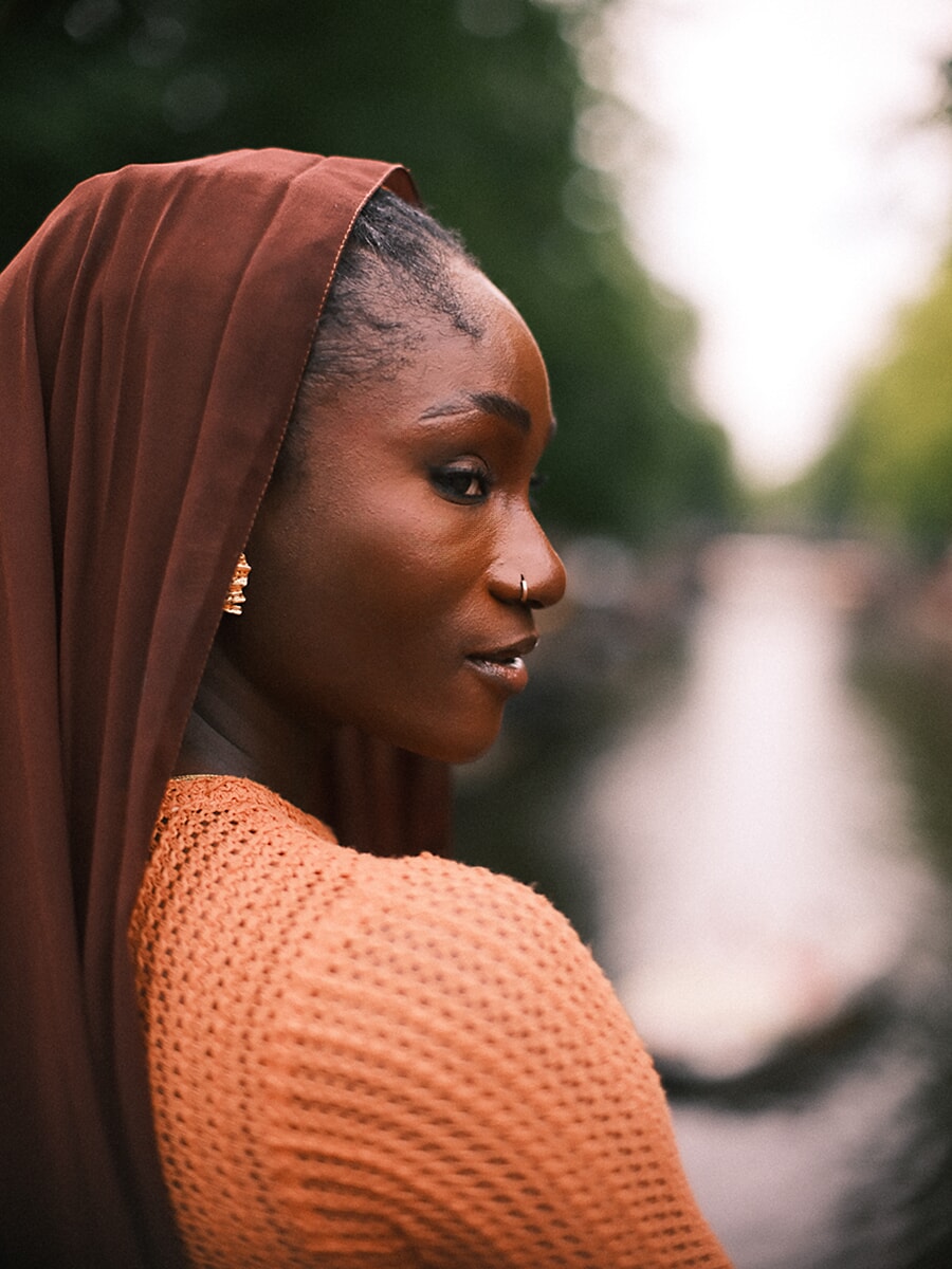 Profiel van een vrouw met roestkleurige hoofddoek die langs de gracht kijkt, een stil moment uit haar creatieve portretsessie