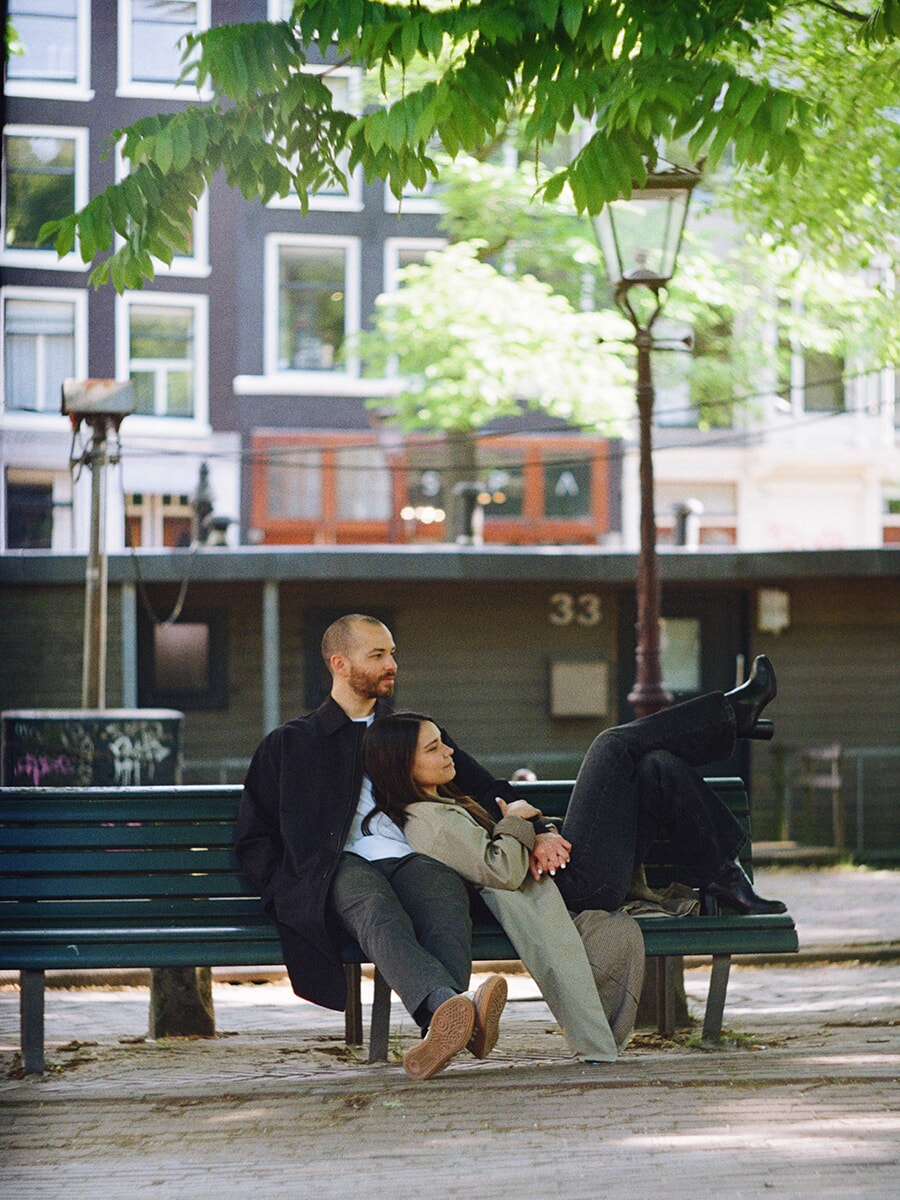 Een stel op een groen bankje aan de gracht in Amsterdam, zij tegen hem aan met haar laarzen omhoog, vastgelegd op kleurenfilm