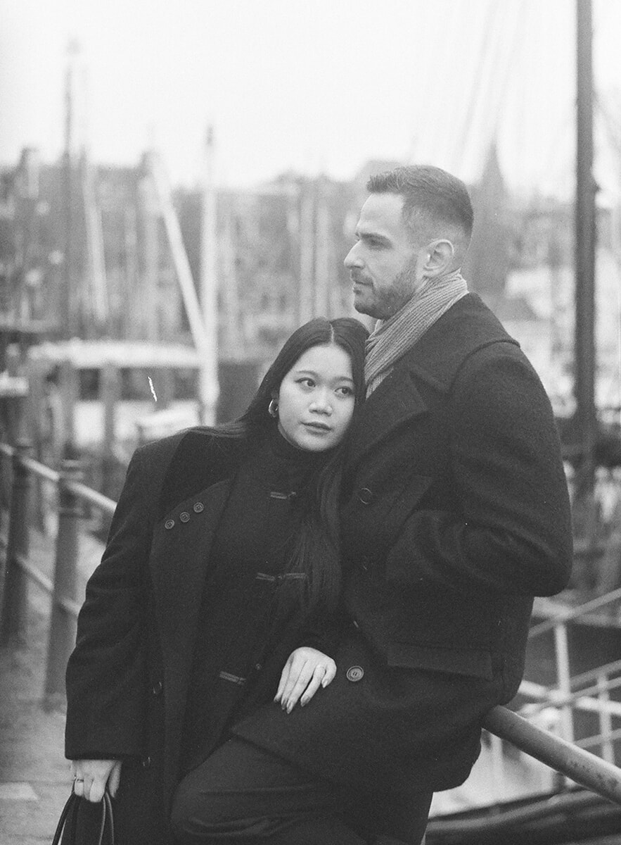 Bij een havenreling leunt een vrouw met haar hoofd tegen haar partner aan, met scheepsmasten op de achtergrond