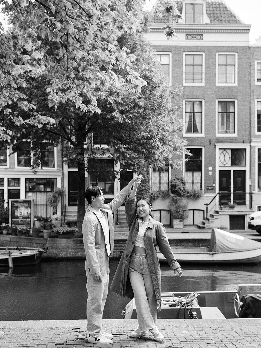 Al draaiend onder de geheven hand van haar partner lacht een vrouw bij de gracht tijdens een analoge fotoshoot in Amsterdam