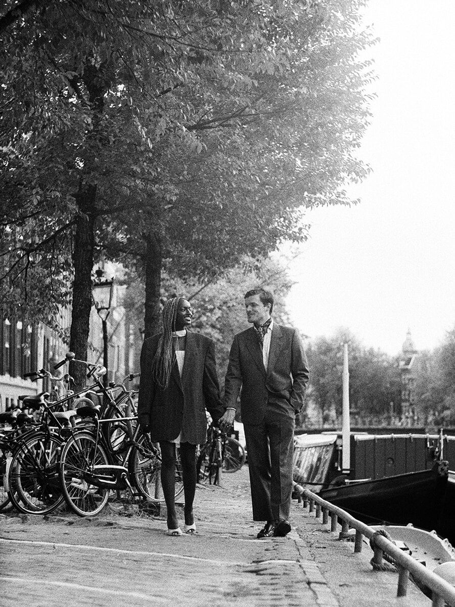 Tijdens een analoge fotoshoot in Amsterdam kijkt een stel elkaar aan terwijl ze hand in hand langs de gracht lopen