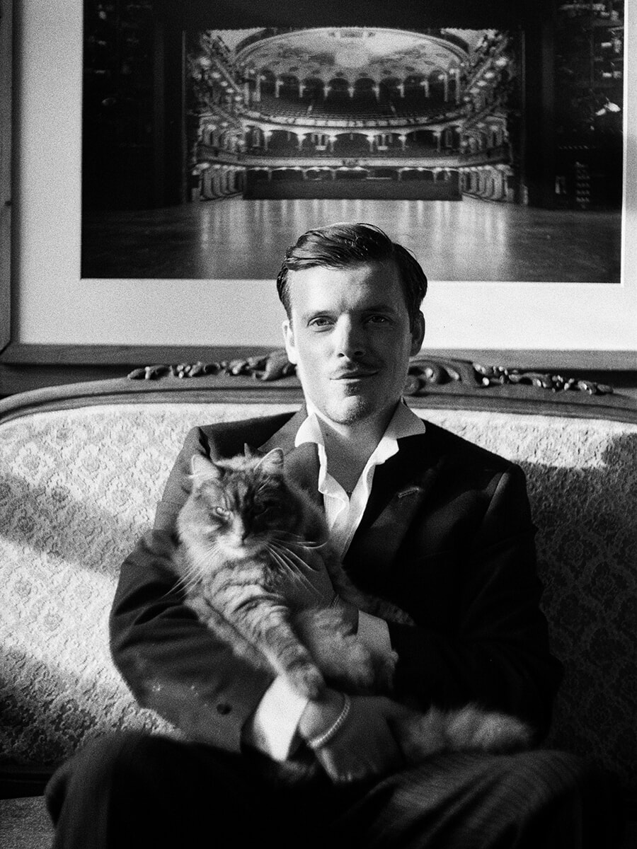 Een man in pak met een kat op schoot op een sierlijke bank, geportretteerd op zwart-witfilm