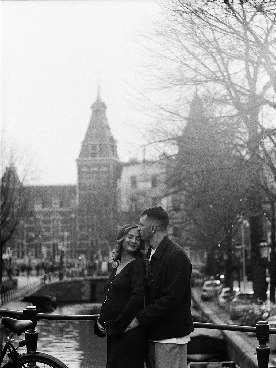 Bij het Rijksmuseum in Amsterdam kust een man zijn zwangere partner op haar voorhoofd tijdens een analoge zwangerschapsfotoshoot