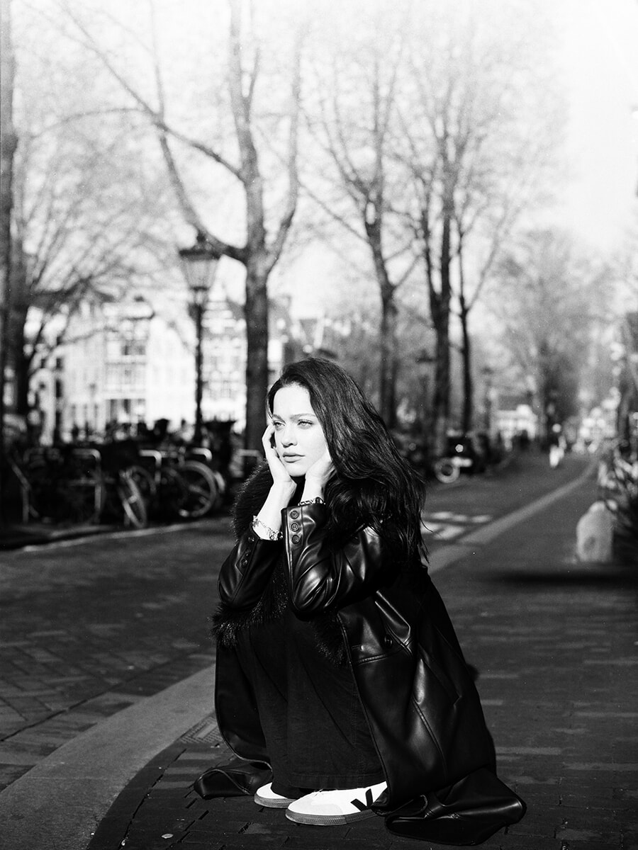 Gehurkt op een stoep in Amsterdam steunt een vrouw haar gezicht in haar handen voor een analoog straatportret